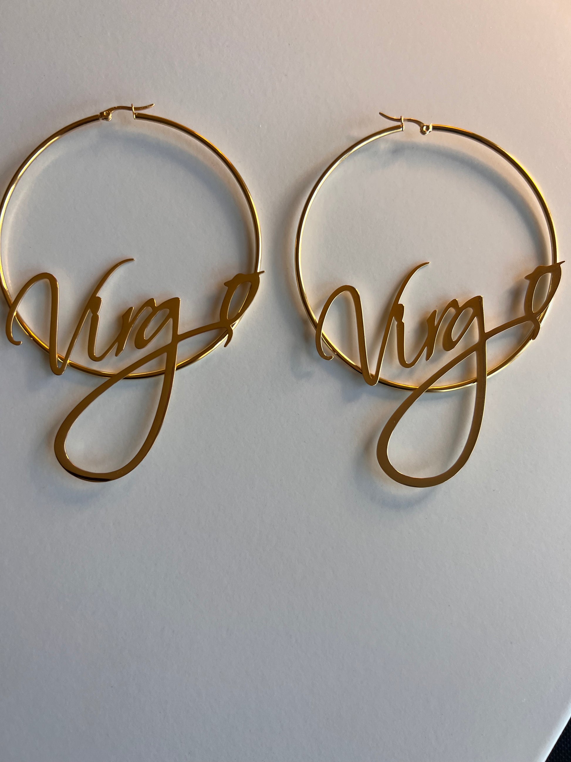 gold hoop earrings with zodiac sign written across the earrings